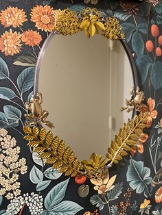 a mirror sitting on top of a wall next to a flowery wallpaper covered in gold leaves