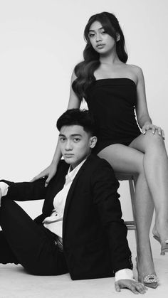 two people are sitting on a chair posing for a black and white photo with their legs crossed