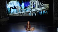 a woman kneeling down next to a dog in front of a large screen with a bridge on it