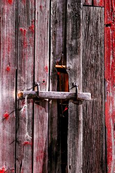 an old wooden door with a bottle on the handle, and red paint peeling from it