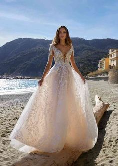 a woman standing on top of a sandy beach wearing a wedding dress with an open back