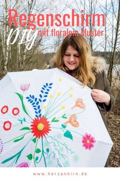 a woman holding an umbrella with flowers painted on it in front of trees and bushes