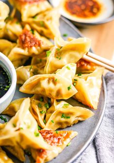 some dumplings are on a plate with sauce and chopsticks next to them