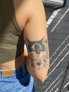 a woman with a cat tattoo on her arm and shoulder, standing in front of a brick wall