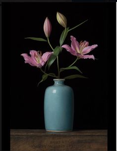 a blue vase filled with pink flowers on top of a wooden table in front of a black background