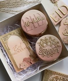 three decorated cupcakes in a box with gold trimming and pink frosting