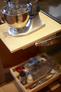 a stand mixer sitting on top of a wooden counter next to an open drawer with utensils in it