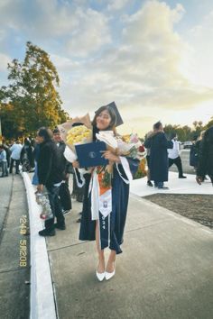 a woman in graduation gown holding a laptop computer on the sidewalk with other people around her