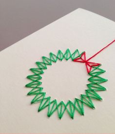 an ornament made out of green thread on a white surface with a red string