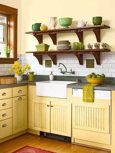 a kitchen with yellow cabinets and green dishes on the shelf above the sink is decorated with flowers