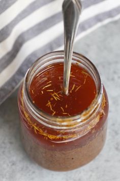 a spoon in a jar filled with some kind of sauce on a counter top next to a striped towel