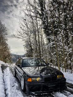 a black car parked on the side of a snow covered road next to some trees