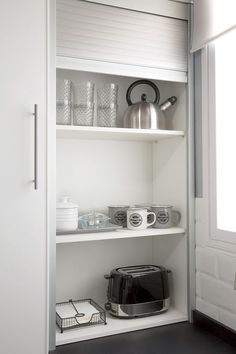 an open cupboard with coffee pots, cups and toaster on it's shelves