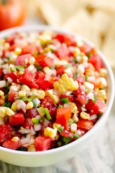 corn and tomato salad in a white bowl on top of a wooden table next to an ear of corn