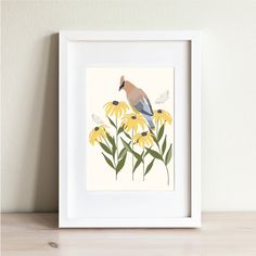 a bird sitting on top of a yellow flower next to a white framed wall hanging