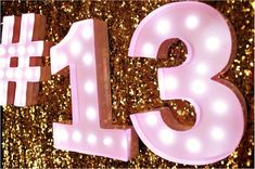 the number thirteen is lit up in front of a gold glitter background with white lights