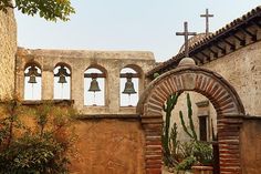 an old church with bells on the roof and cactus in the foreground, surrounded by stone walls