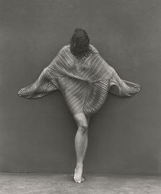 a black and white photo of a woman standing in front of a wall with her arms stretched out