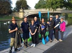 a group of people standing on the side of a river holding paddles and poles