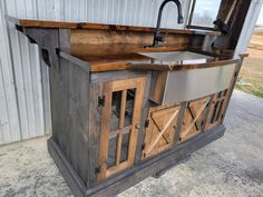 an outdoor kitchen made out of wood and metal with a sink, counter top, and cupboards