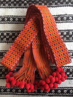 an orange scarf with red pom poms on the bottom and black and white striped background