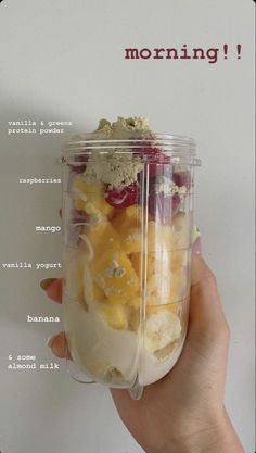 a person holding up a plastic container filled with fruit and yogurt in front of a white background