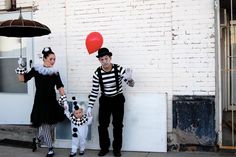 two people dressed as clowns holding balloons and standing next to a white brick building