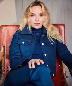 a woman sitting in a chair wearing a blue coat