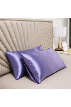 two purple pillows sitting on top of a bed next to a nightstand with a lamp