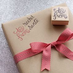 a gift wrapped in red and white ribbon next to a rubber stamp with the word santa written on it