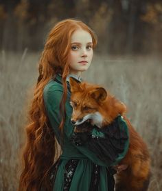 a woman with long red hair holding a fox in her arms and looking at the camera