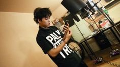 a young man standing in front of a lamp looking at his cell phone while wearing a t - shirt that says play music