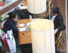 two people sitting at a table in a restaurant talking on their cell phones and eating