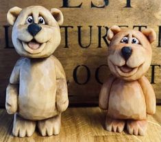 two clay bears sitting next to each other on a wooden table with a sign in the background