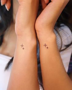 two girls with matching tattoos on their arms, one is holding her hand up to the other