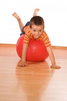 a young boy laying on top of a red ball in the middle of a room