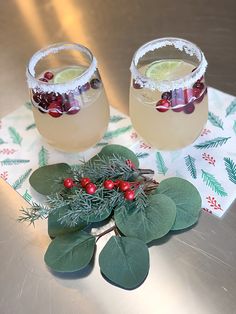 two glasses filled with drinks sitting on top of a table next to leaves and holly