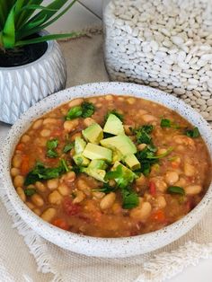 a white bowl filled with beans and avocado on top of a table next to a potted plant