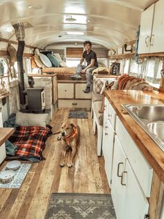 a man sitting in the kitchen next to a dog on a wooden floor near a sink and stove