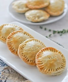 three small pies on a white plate next to some green sprig leaves