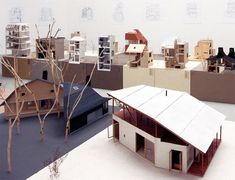 a group of cardboard houses sitting on top of a floor next to trees and buildings