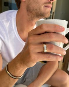 a man is holding a cup and looking at something in his hand while wearing a ring