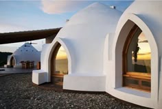 a white building with two arched windows on top of it's roof and the ocean in the background