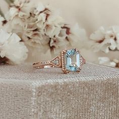 a ring with an aqua blue topazte surrounded by white and pink flowers on a table