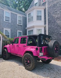 a pink jeep is parked in front of a house with two large tires on it