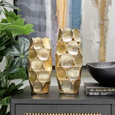 two gold vases sitting on top of a table next to a book and plant