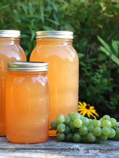 three jars filled with liquid sitting next to grapes