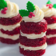 three small red velvet cakes with white frosting and holly leaves on top, sitting on a plate