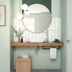 a bathroom with green walls and white tile on the floor, along with a round mirror