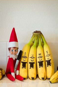 an elf is sitting next to bananas with faces drawn on them and the other two are holding pens